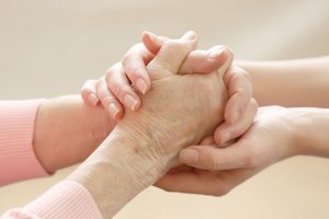 mantelzorger en oudere dame die handen aan elkaar geven